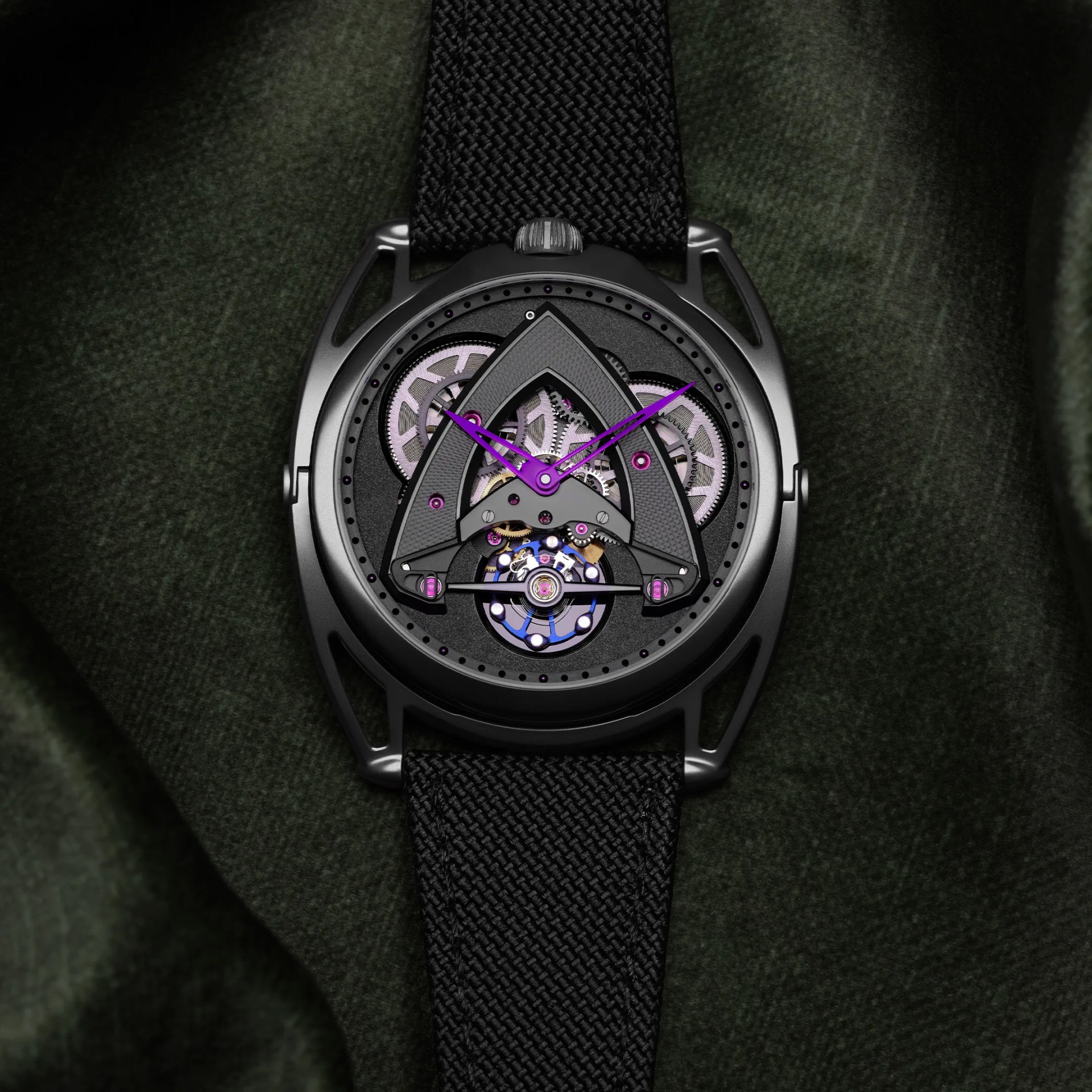 Black wristwatch with purple hands and visible mechanical gears on a dark green fabric background.