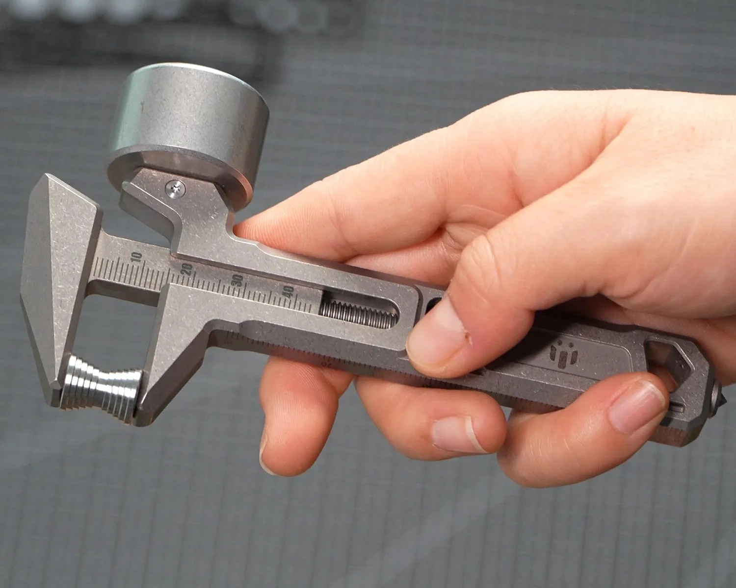 Hand holding a metal adjustable wrench with a cylindrical attachment on the jaw.