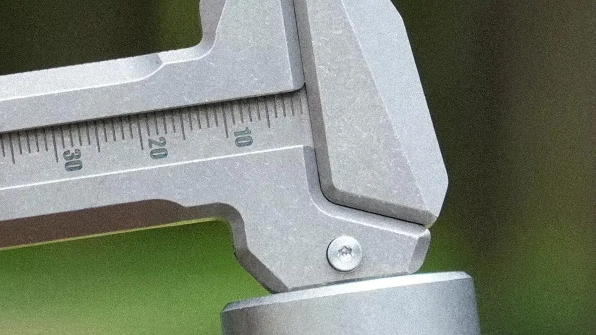 Close-up of a metal caliper measuring a cylindrical object with visible measurement markings.
