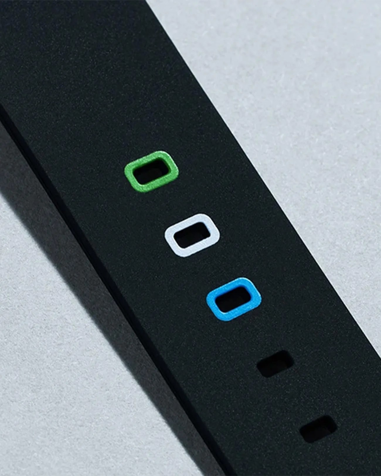 Black strap with rectangular holes outlined in green, white, and blue on a light surface.