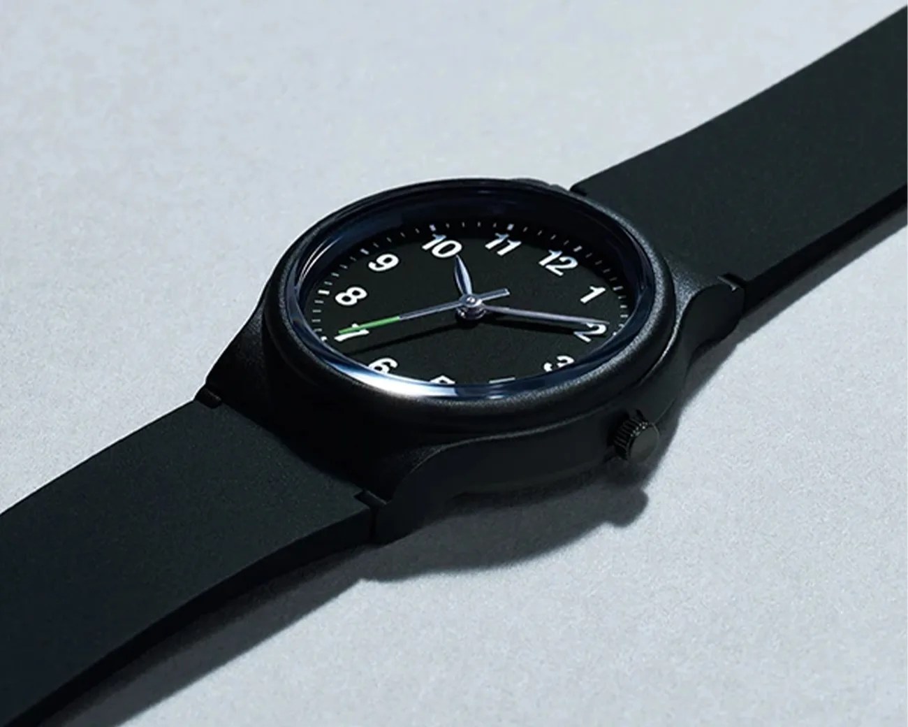 Black analog wristwatch with white numerals and a black silicone strap on a light surface.