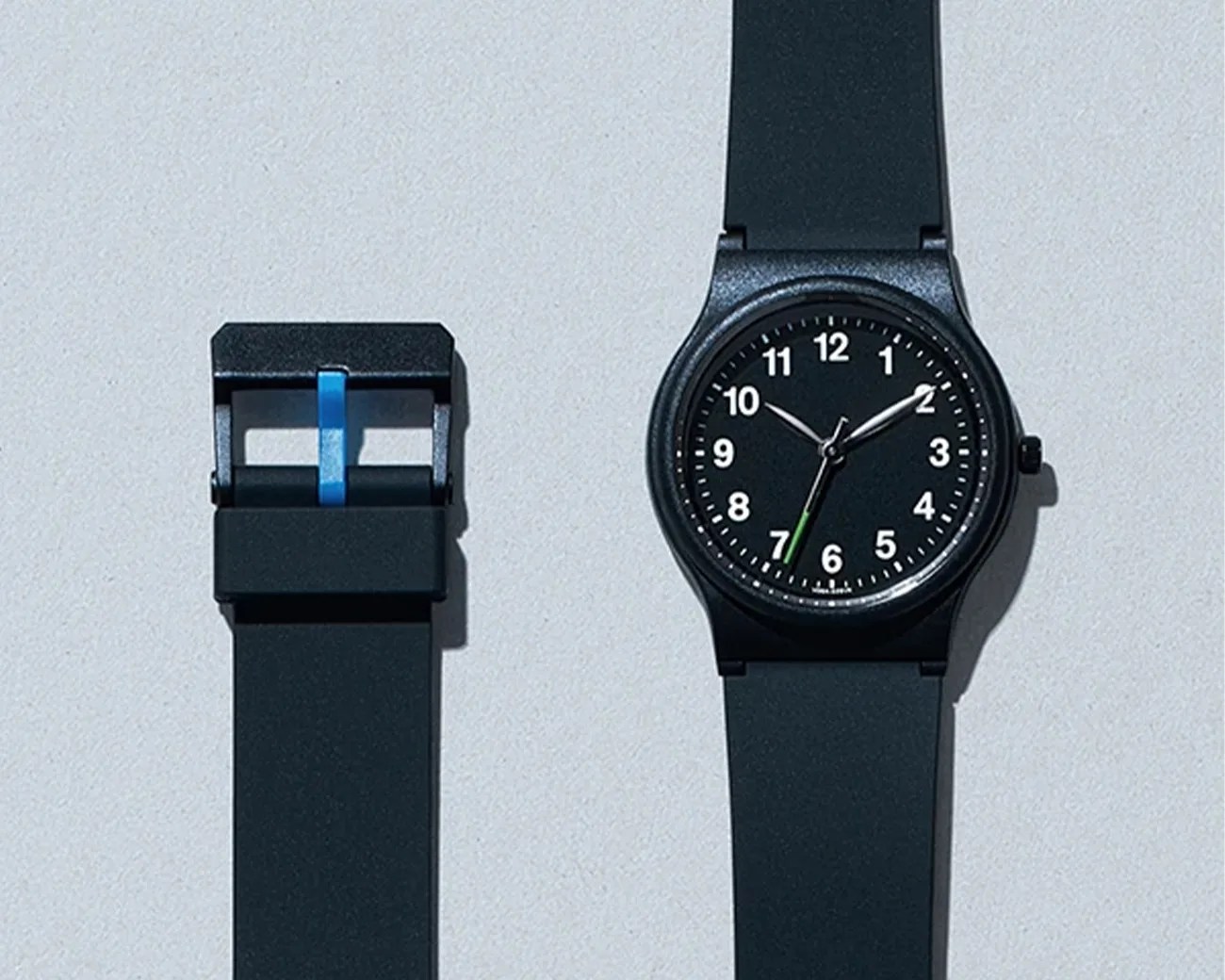 Black analog wristwatch with white numbers and a black strap, shown with the strap buckle detached.