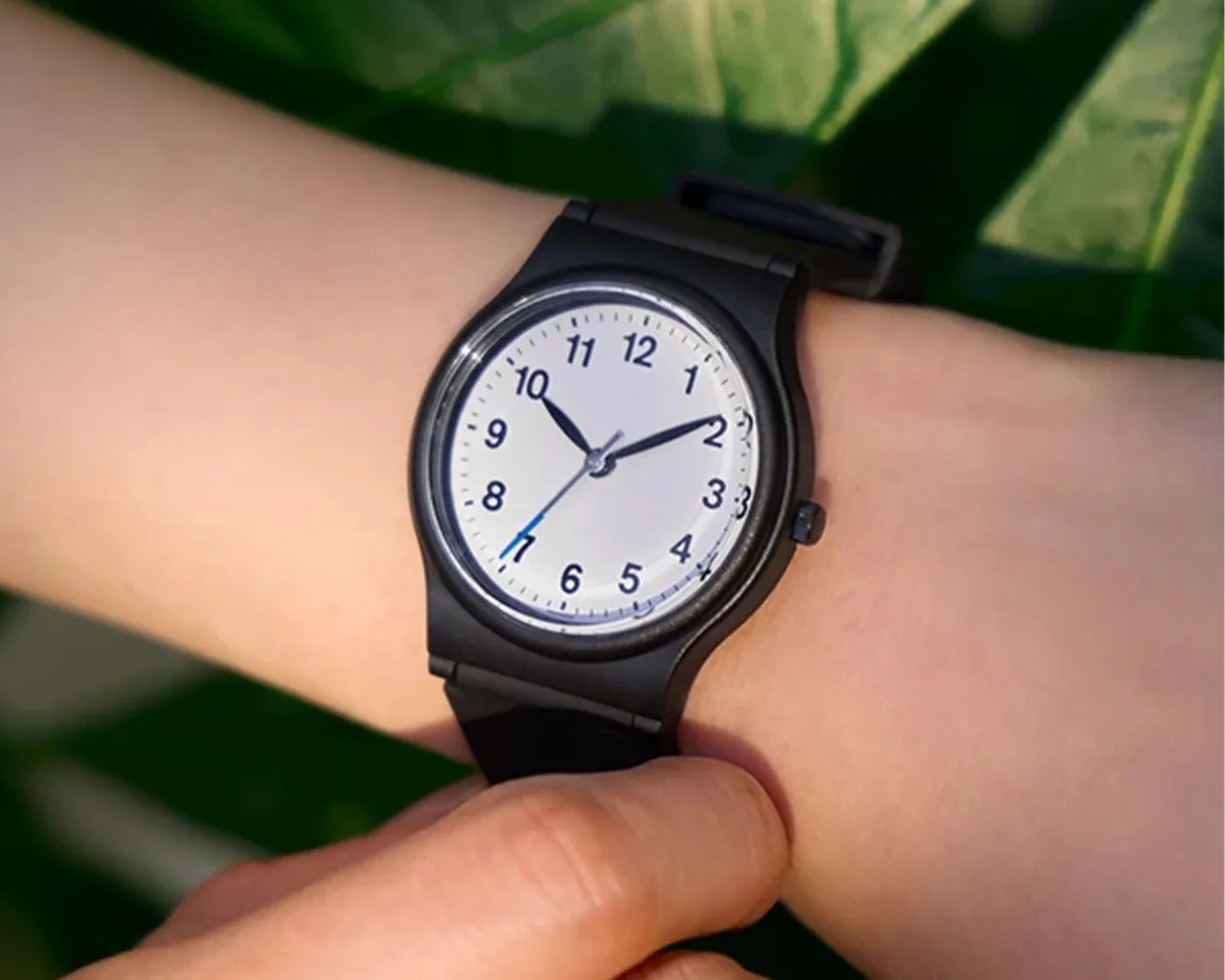 Black wristwatch with a white dial and black numerals worn on a wrist outdoors.
