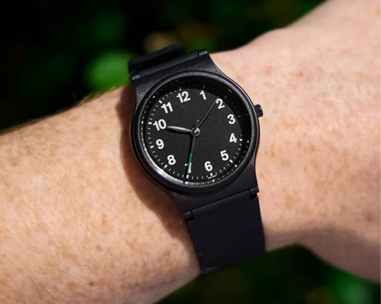 Black analog wristwatch with white numbers and a black strap worn on a wrist.