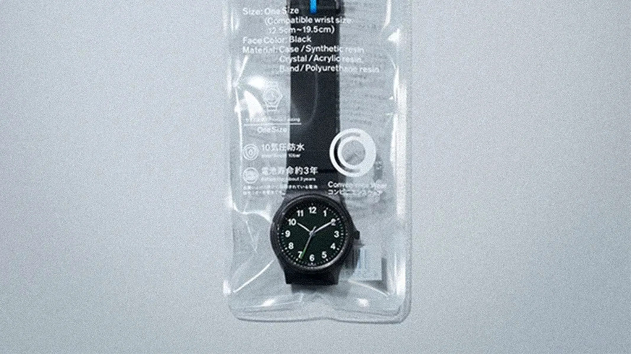 Black analog wristwatch with white numbers and green second hand in clear plastic packaging.
