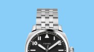 Silver metal wristwatch with black dial and white numerals and hands on a blue background.
