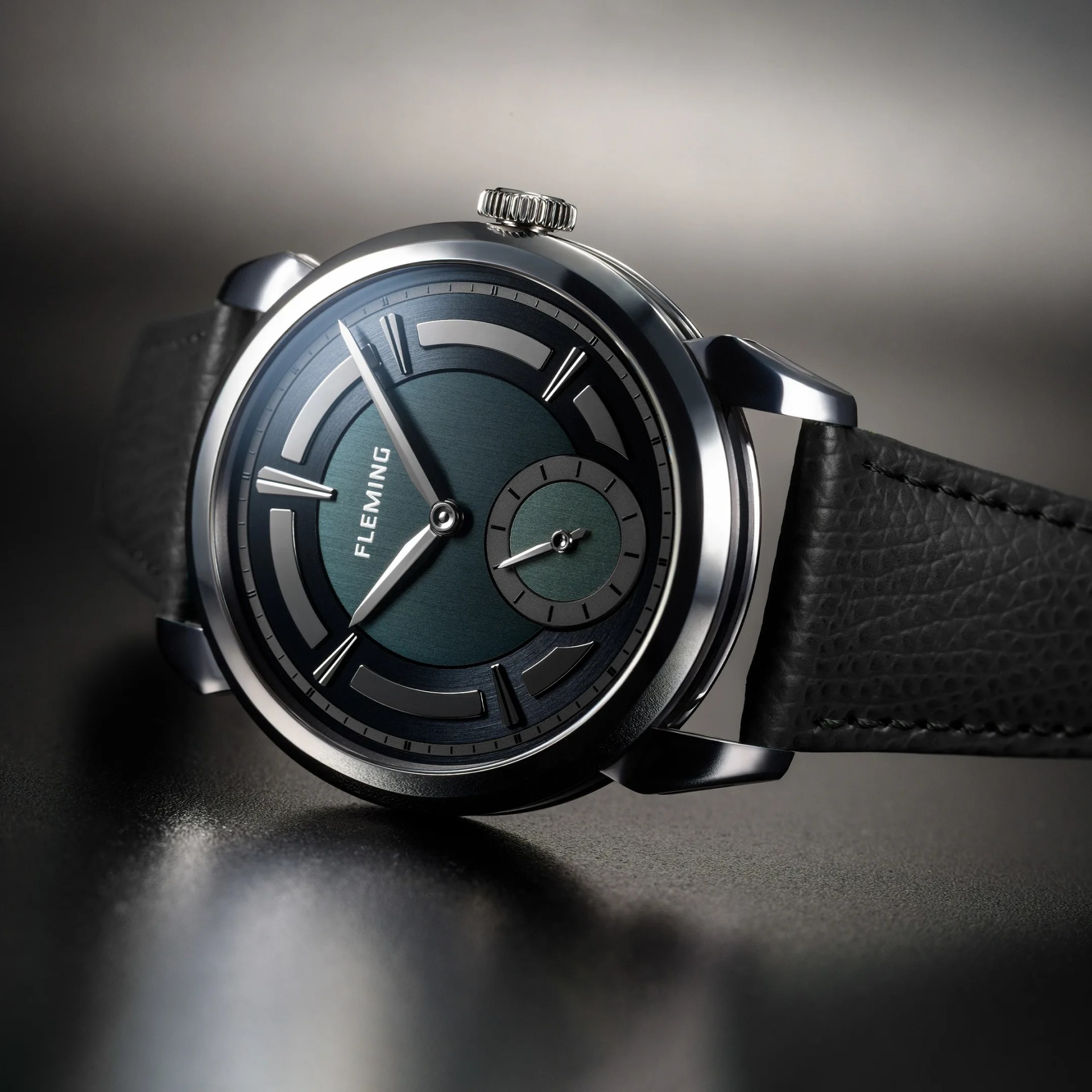 Round silver watch with dark green dial, black leather strap, and "FLEMING" logo on the face.