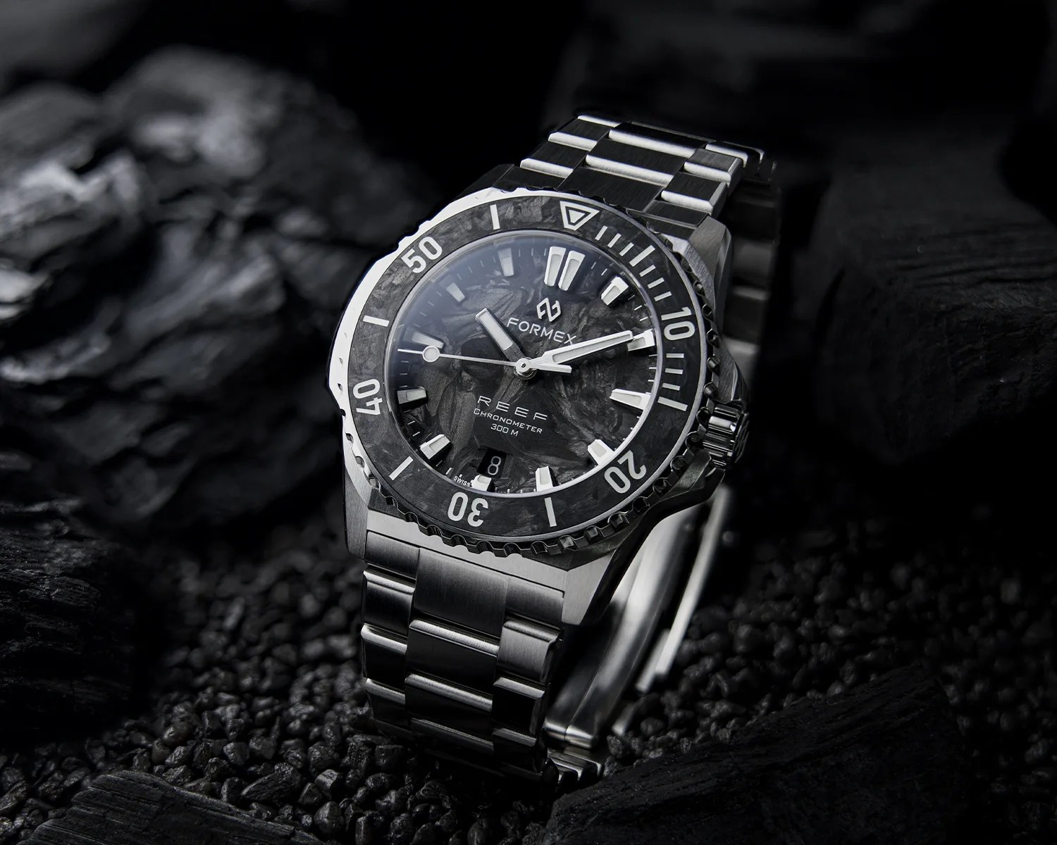 Stainless steel Formex Reef chronometer watch with black textured dial and rotating bezel on black stones.