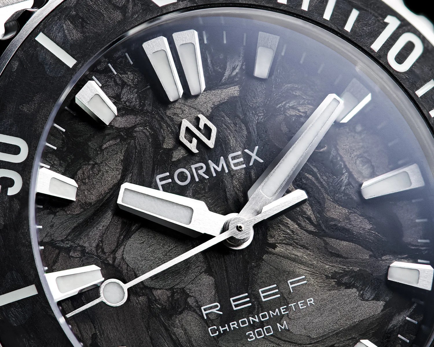 Close-up of a Formex Reef chronometer watch face with silver hands and markers on a textured black dial.