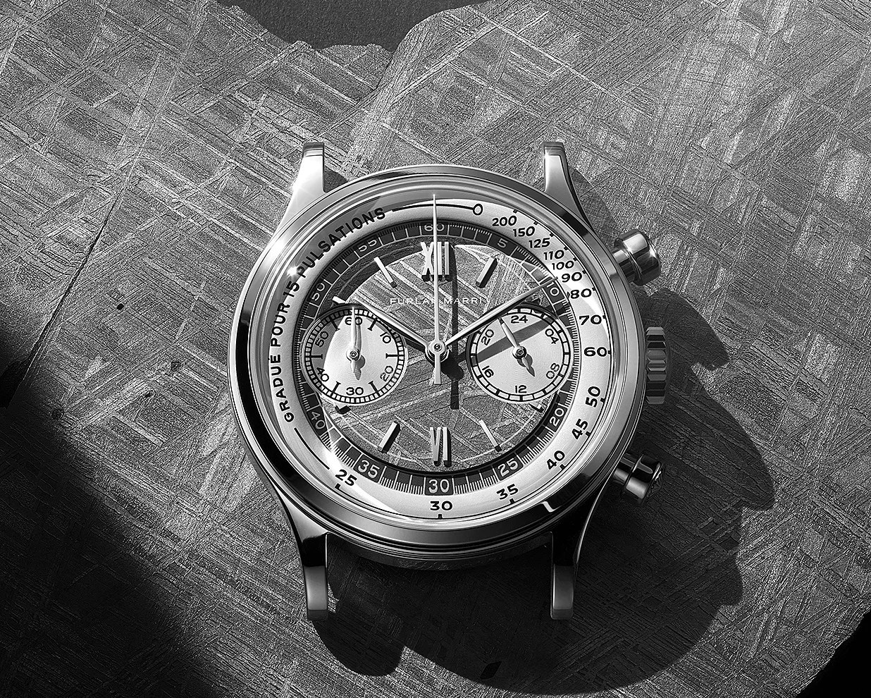 Silver chronograph wristwatch with two subdials and tachymeter scale on a textured metallic surface.