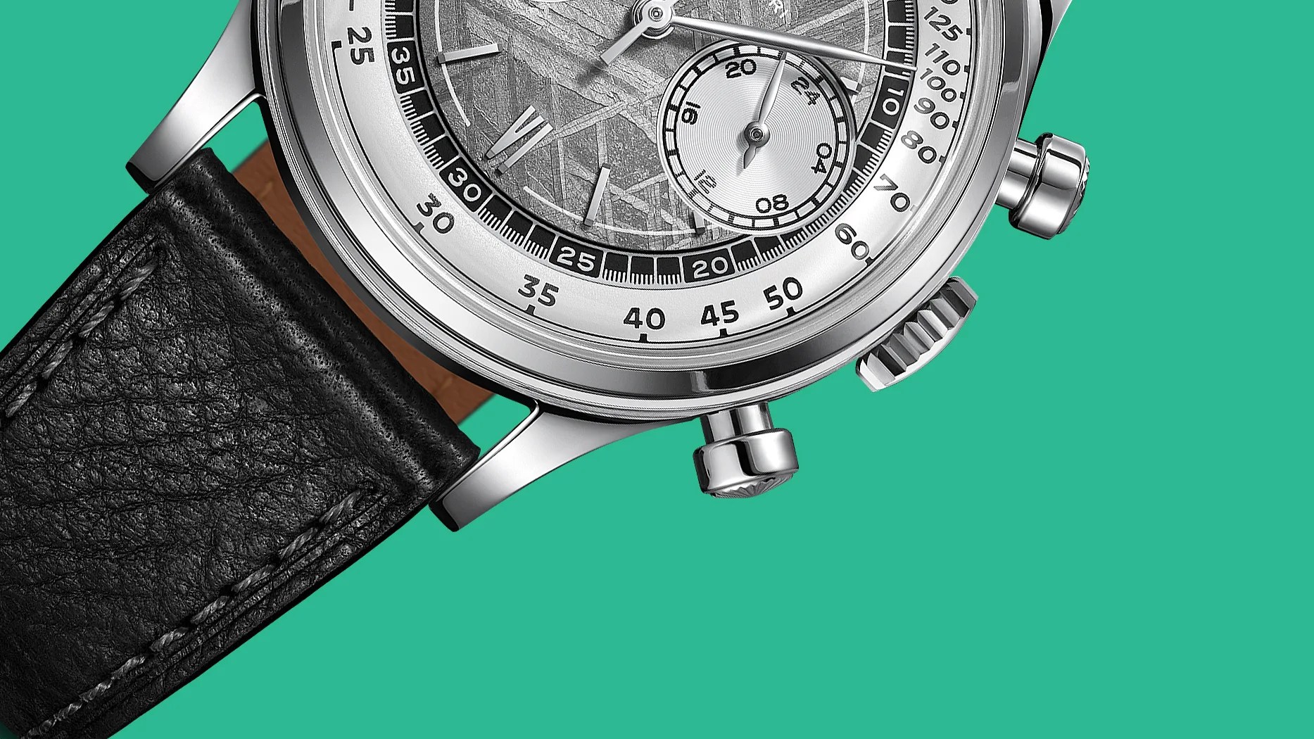 Close-up of a silver chronograph watch with a textured dial, black leather strap, and two push buttons on a teal background.