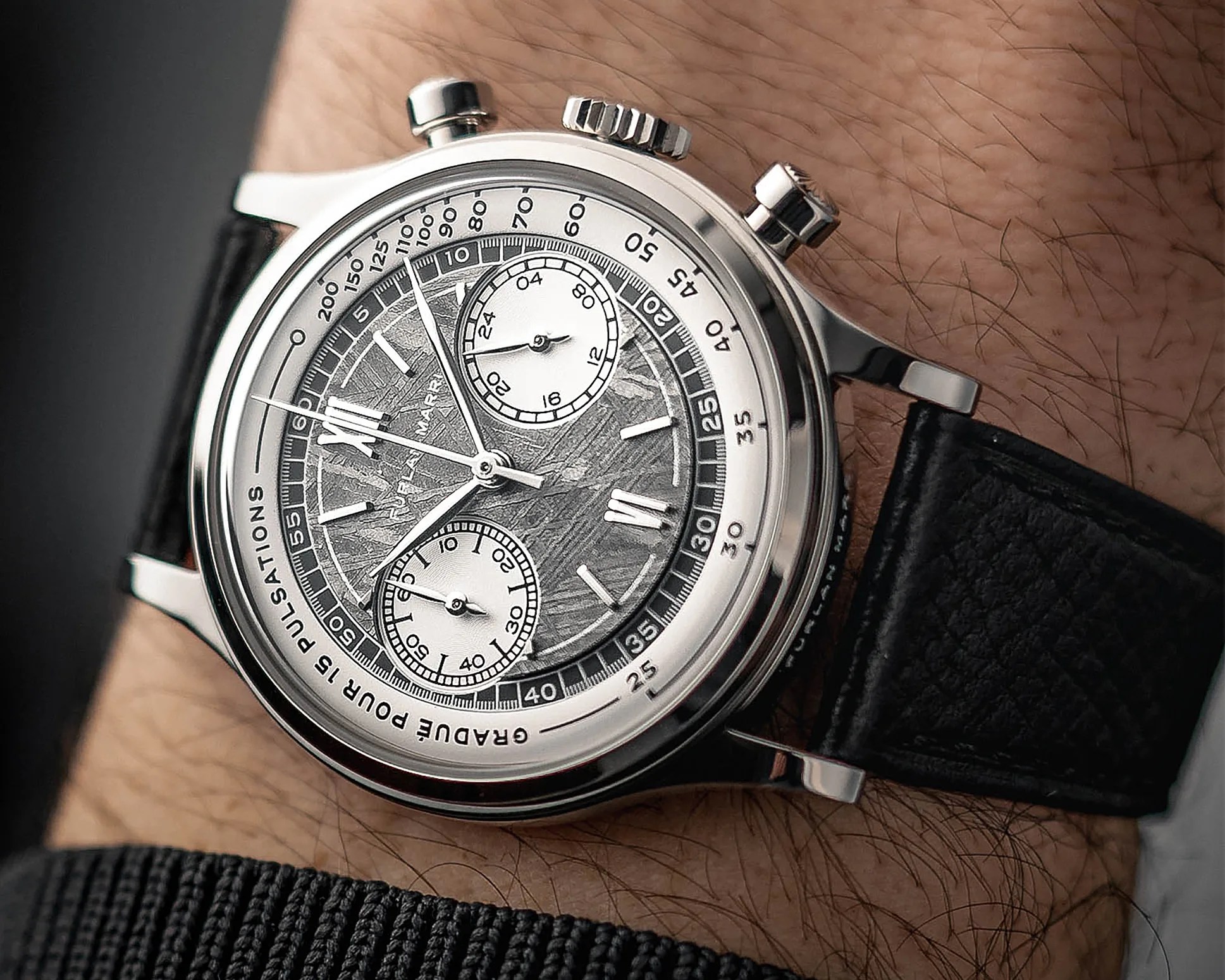 Silver chronograph wristwatch with textured gray dial and black leather strap worn on a wrist.