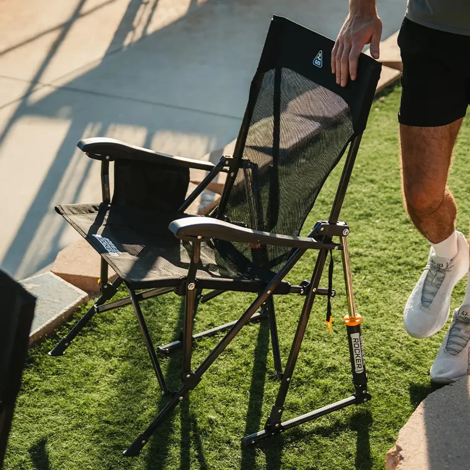 Black mesh folding chair with armrests and a built-in pump labeled "ROCKER" on grass.