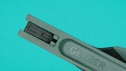 Close-up of a green Gerber multitool with a black component on a turquoise background.