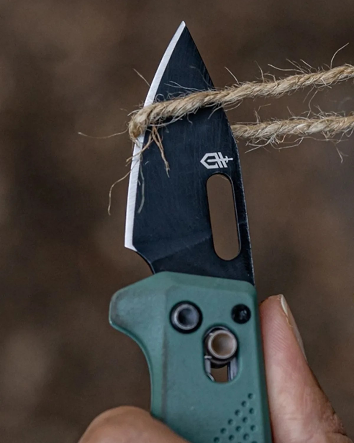 Green-handled folding knife with black blade cutting a piece of twine.