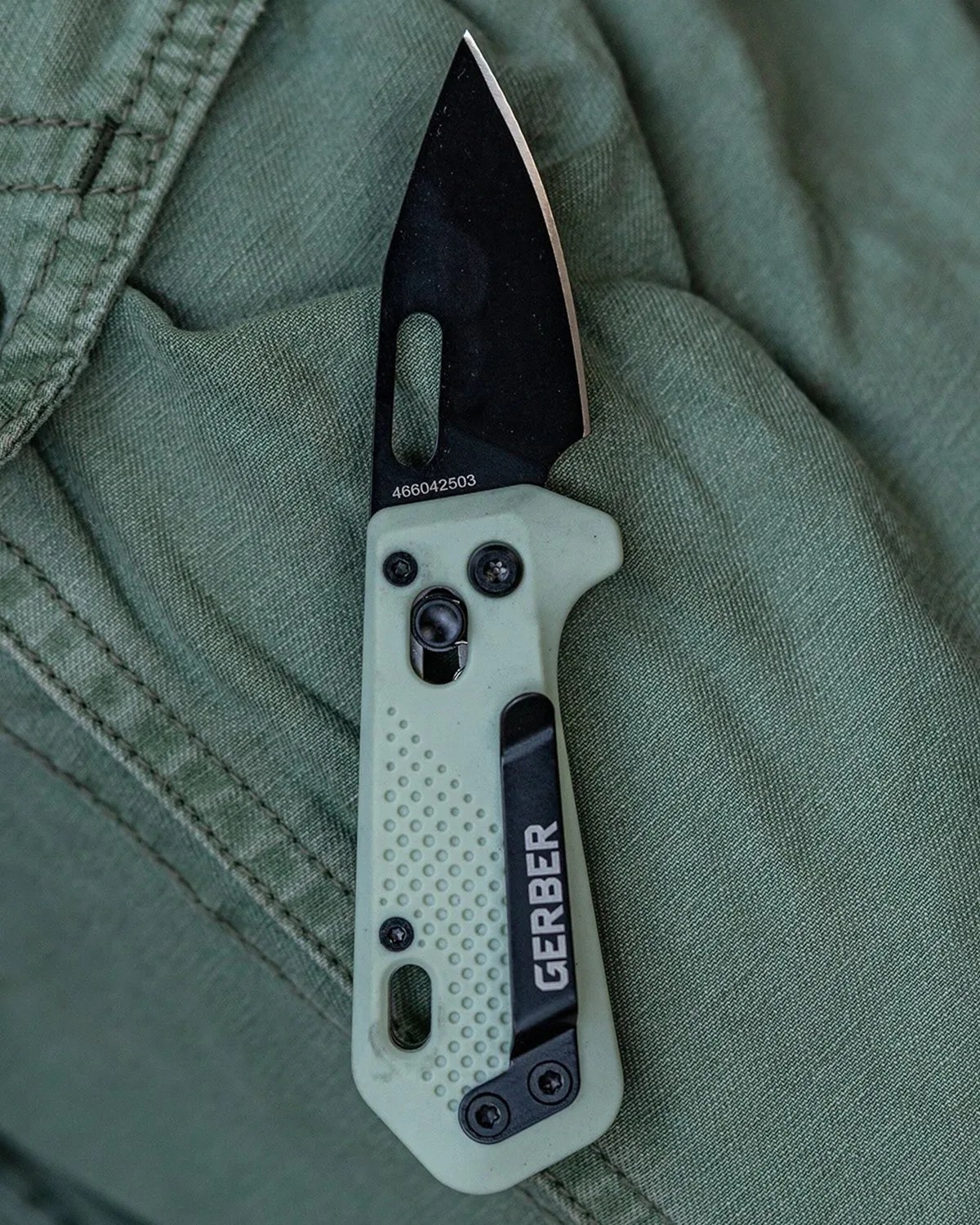 Folding Gerber knife with black blade and light green textured handle on green fabric.