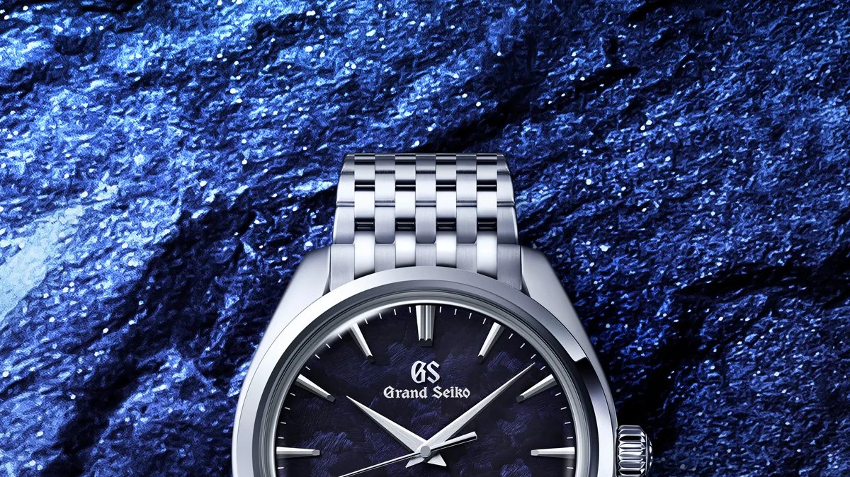 Silver Grand Seiko wristwatch with a textured dark blue dial and metal link bracelet on a blue textured background.