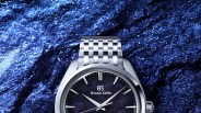 Silver Grand Seiko wristwatch with a textured dark blue dial and metal link bracelet on a blue textured background.