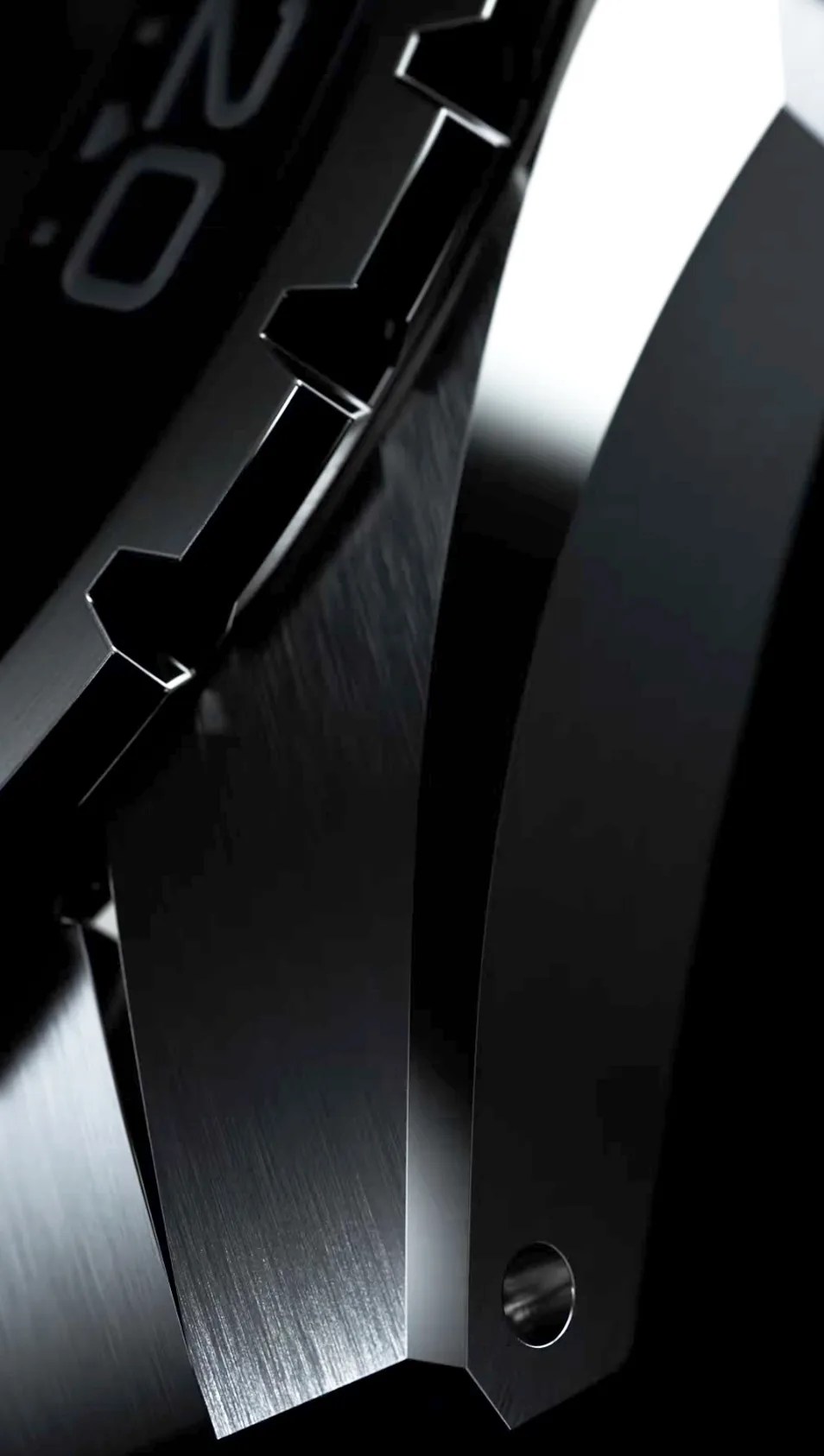 Close-up of a black brushed metal watch bezel with angular edges and a small circular hole.