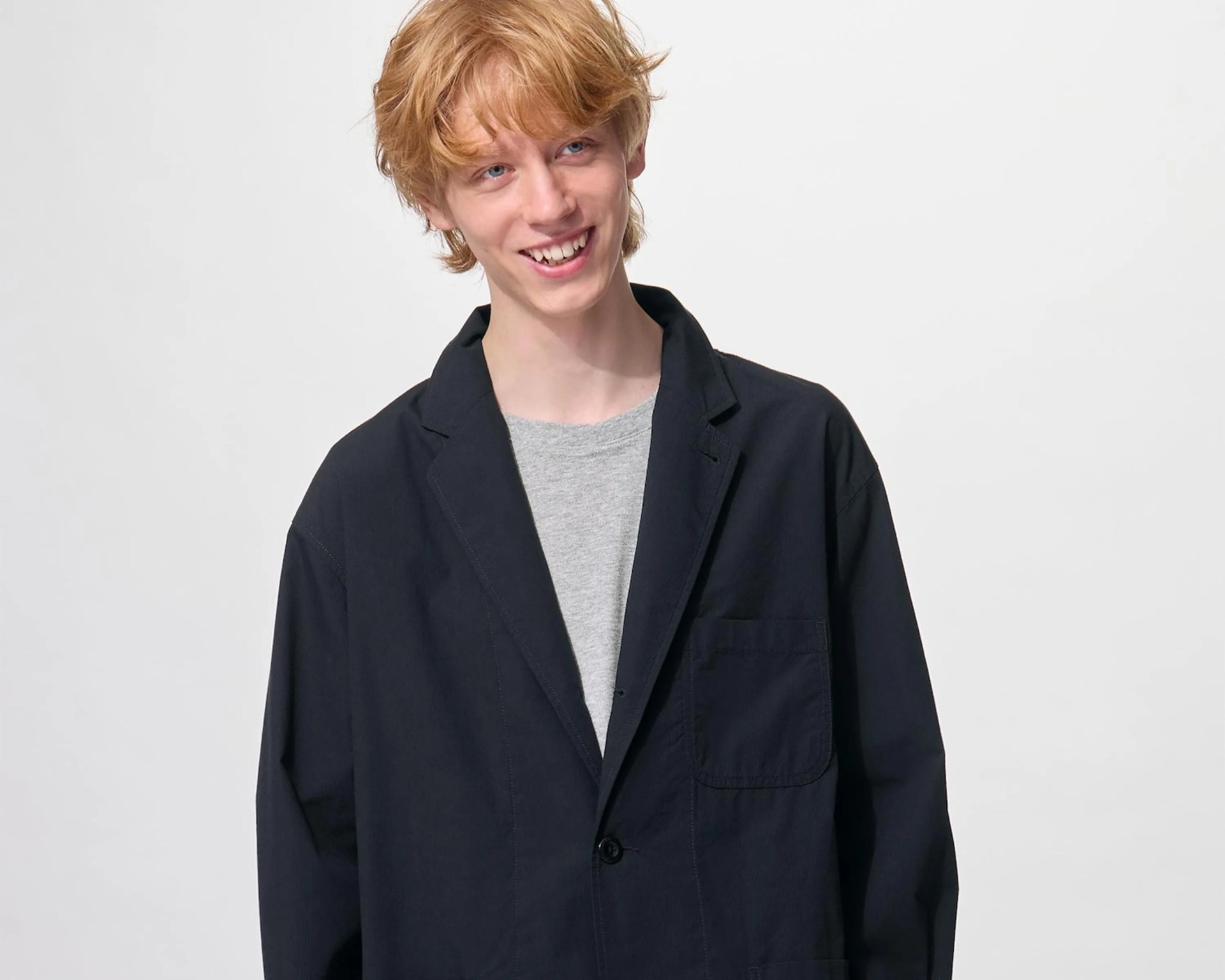 Person wearing a loose-fitting black blazer over a light gray crew neck shirt against a plain white background.