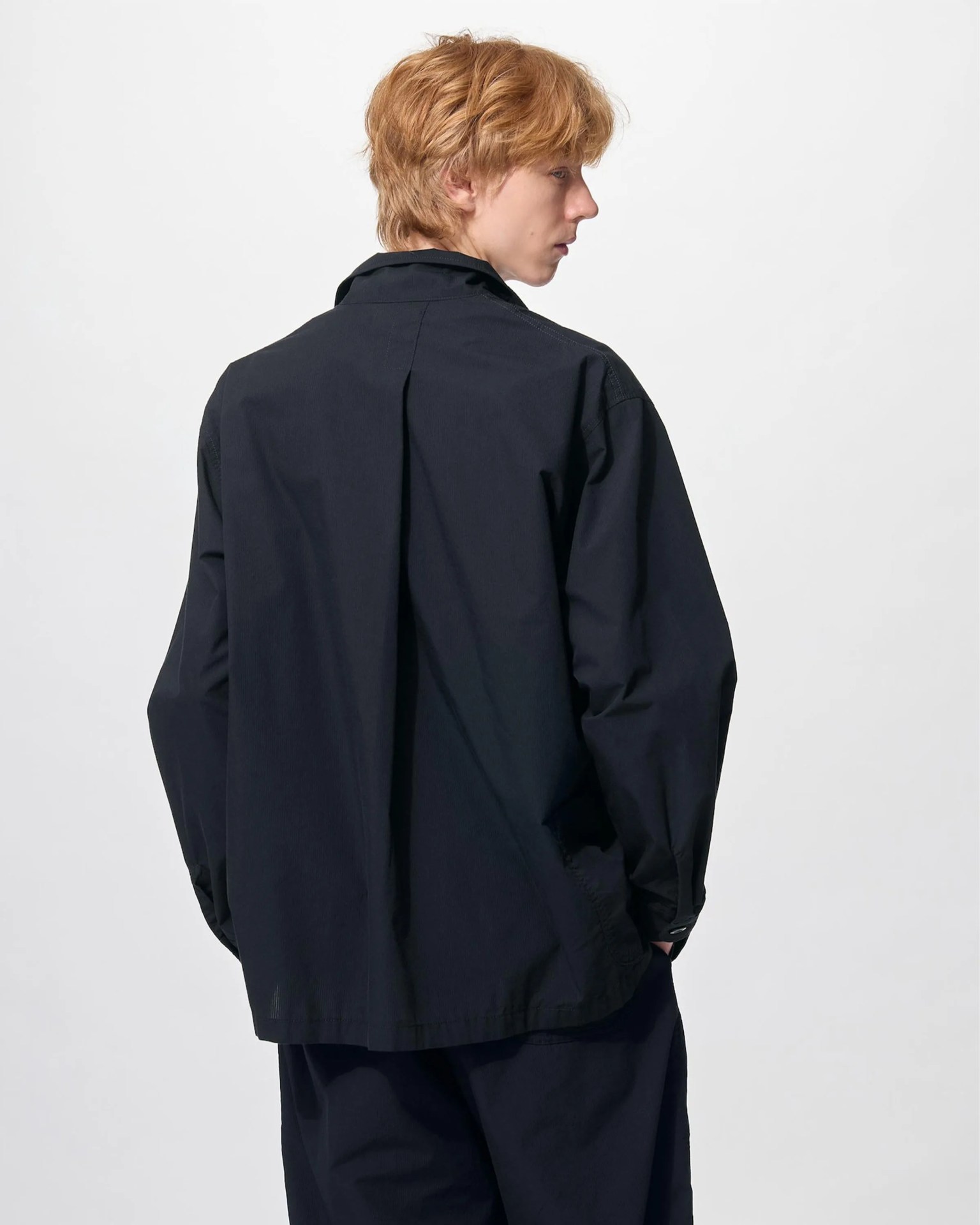 Person wearing a loose-fitting black long-sleeve shirt viewed from the back against a plain white background.