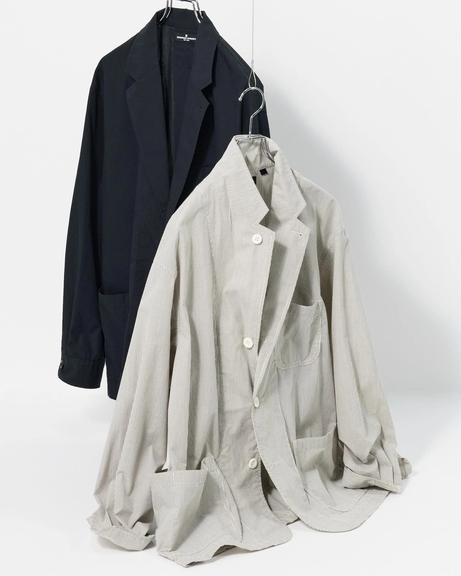 Two oversized blazers hanging on metal hangers, one black and one light beige with thin vertical stripes and white buttons.