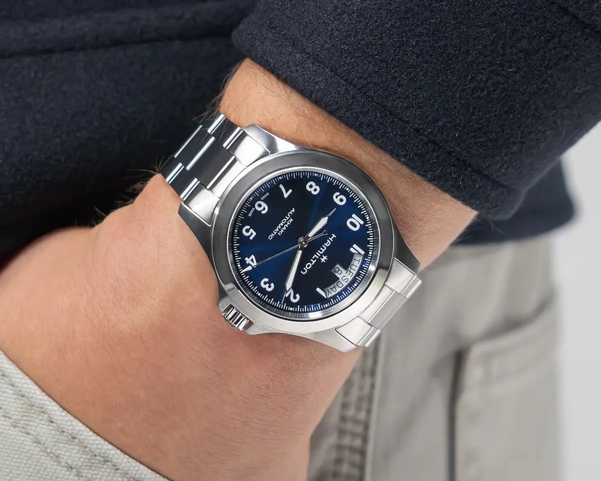 Silver Hamilton wristwatch with a blue dial, white numerals, and day-date display worn on a wrist.