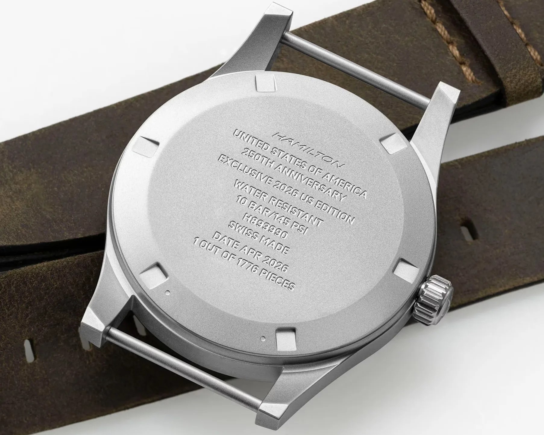 Silver Hamilton watch case back with engraved text and brown leather strap in a hand.