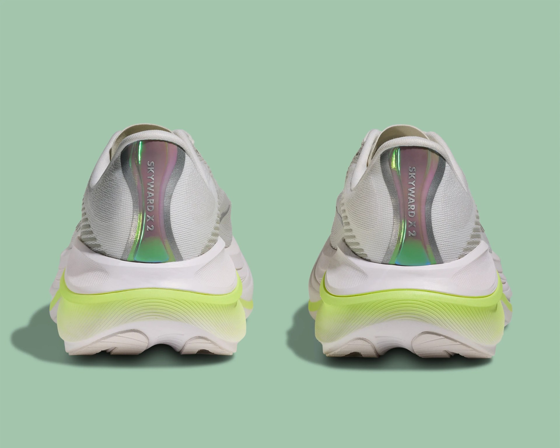 Pair of white running shoes with neon yellow midsoles and iridescent heel tabs labeled "SKYWARD X 2" on a green background.