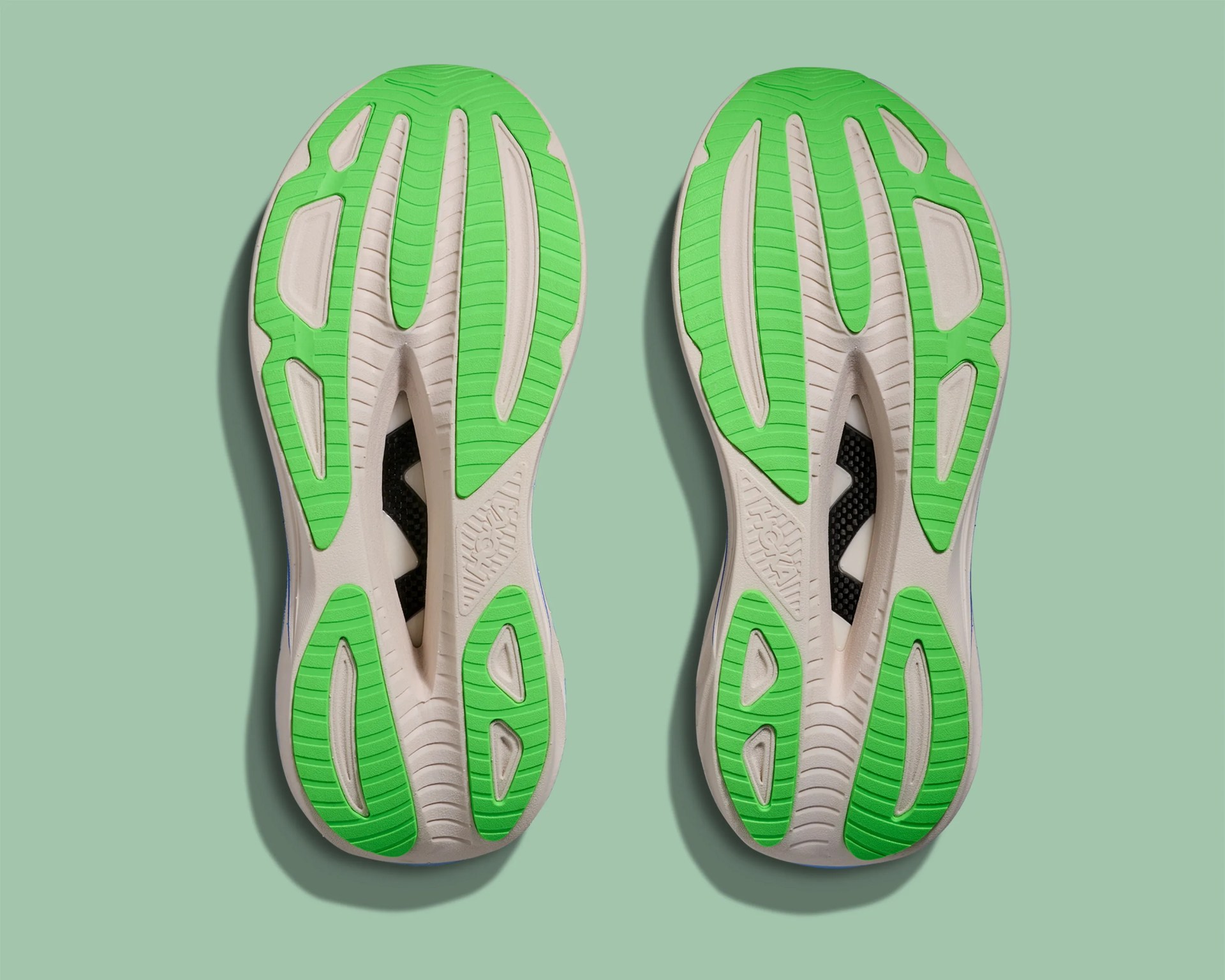 Pair of athletic shoe soles with green and beige rubber tread on a light green background.