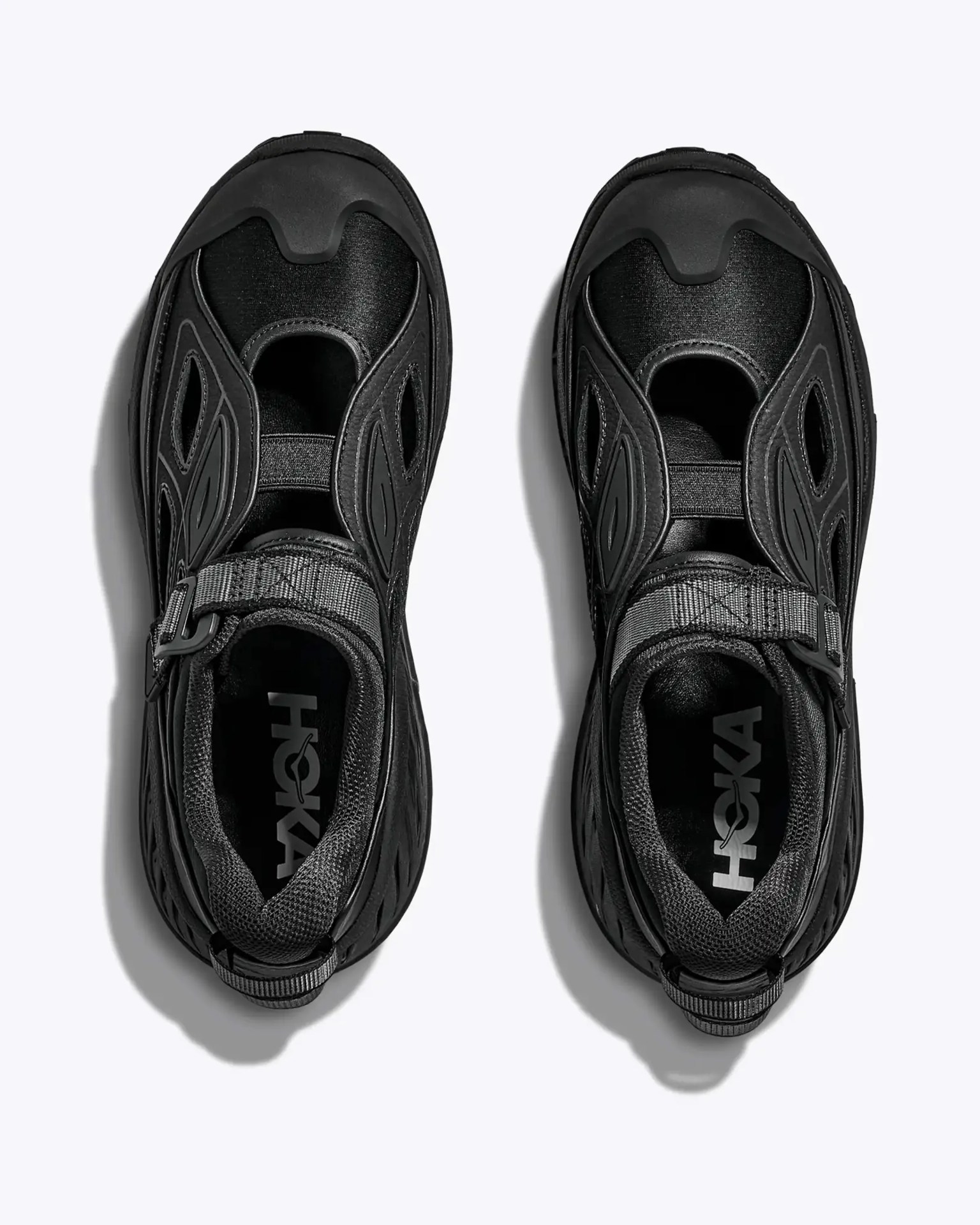 Pair of black HOKA slip-on shoes with cutout details and adjustable straps, viewed from above.