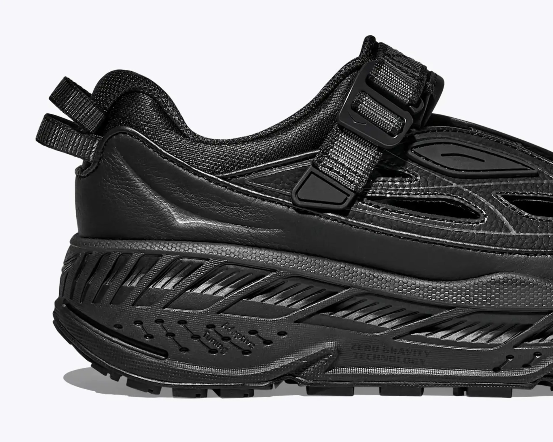 Close-up of the black athletic shoe's heel and midsole with textured synthetic and mesh materials and a strap buckle.