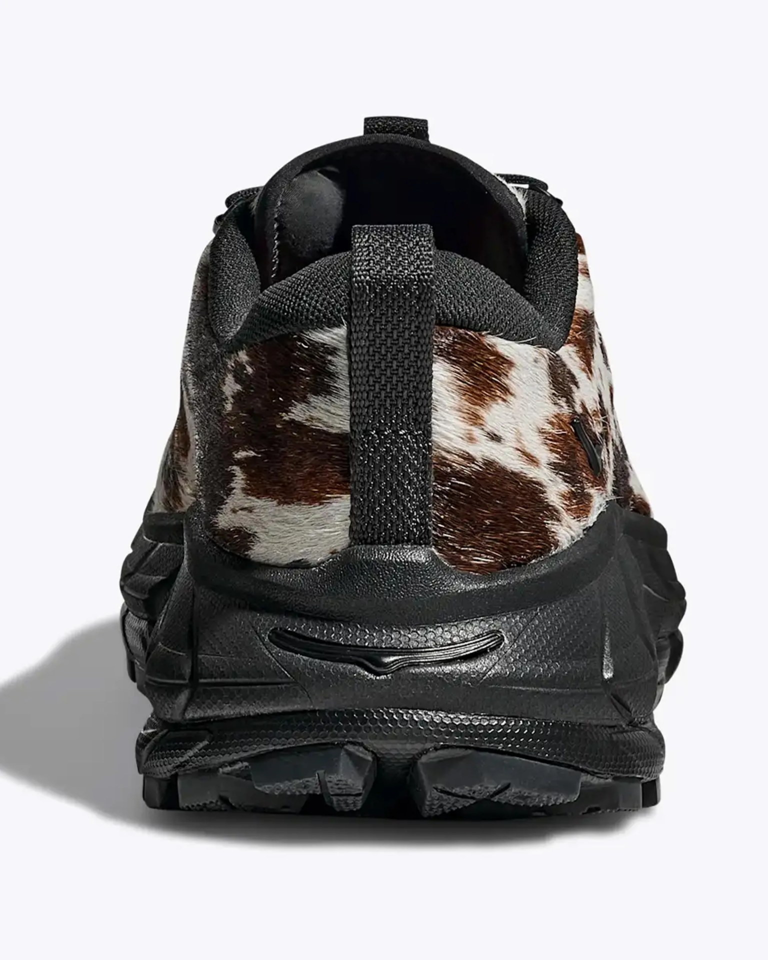 Black sneaker with brown and white cowhide pattern on the upper, viewed from the back.