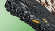 Close-up of a black Vibram shoe sole with deep treads and yellow Vibram logo on a green background.