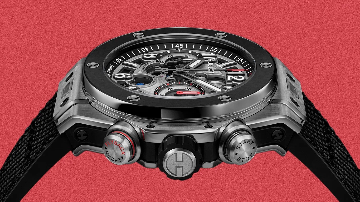 Close-up of a Hublot wristwatch with a black and silver case, skeleton dial, and black textured strap against a red background.