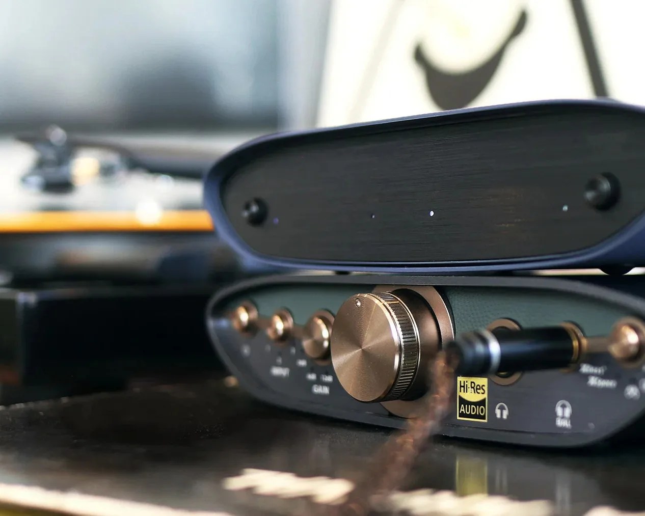 Close-up of a black audio amplifier with gold knobs and a large volume dial on a reflective surface.