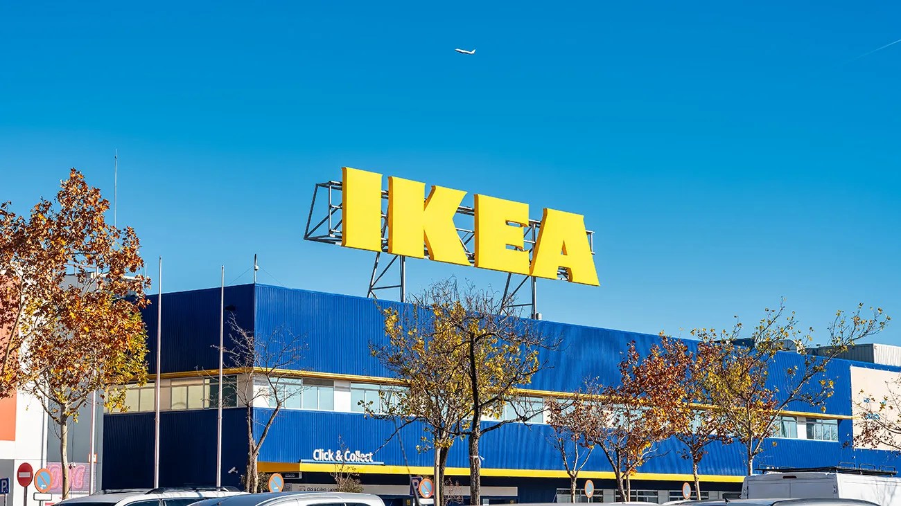 Large yellow IKEA sign on top of a blue building with autumn trees and parked cars below.