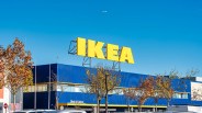 Large yellow IKEA sign on top of a blue building with autumn trees and parked cars below.