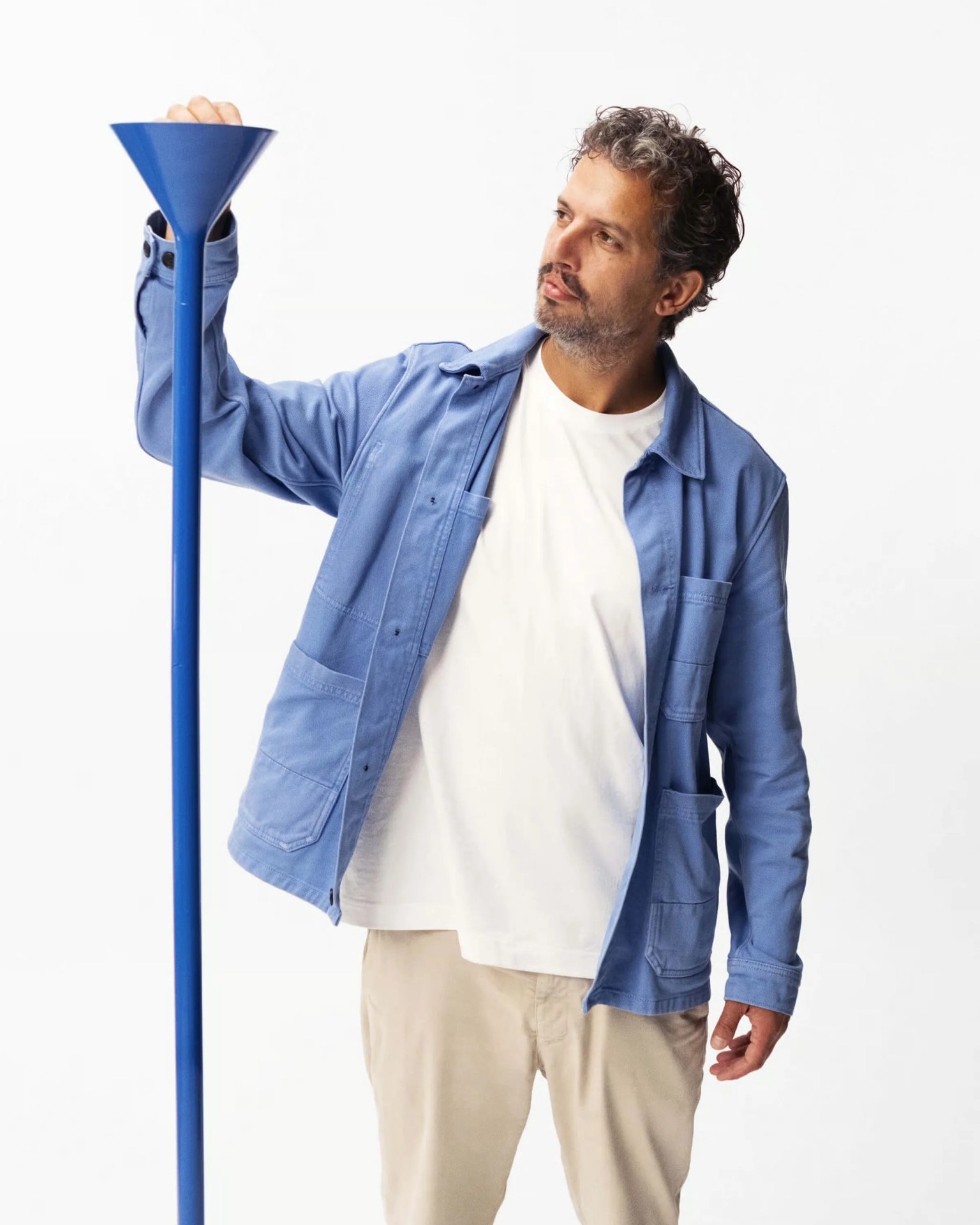 Man wearing a light blue jacket and white shirt holding a tall blue funnel against a white background.