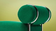 Green upholstered cylindrical headrest with chrome metal supports on a matching green sofa.