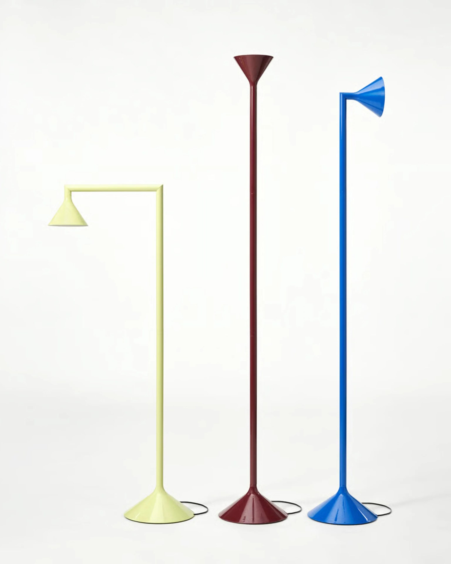 Three modern metal floor lamps in pale yellow, burgundy, and blue with conical bases and shades on a white background.