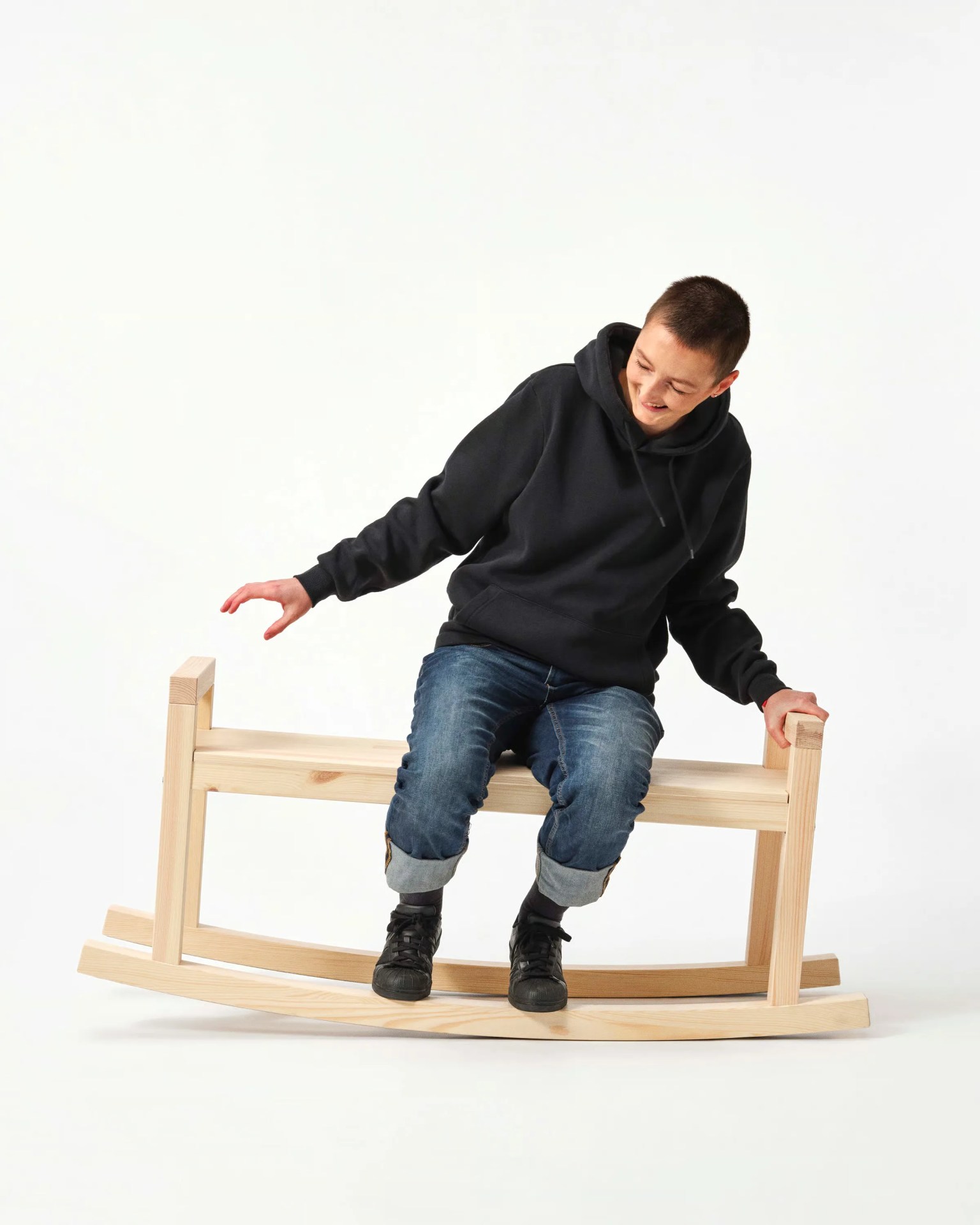Person wearing a black hoodie and rolled-up jeans sitting on a light wooden rocking chair.