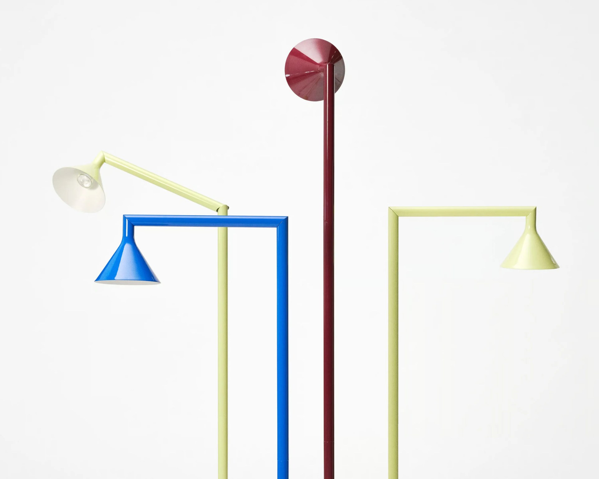 Three modern floor lamps with conical shades, one blue with yellow arm, one yellow, and one burgundy, against a white background.
