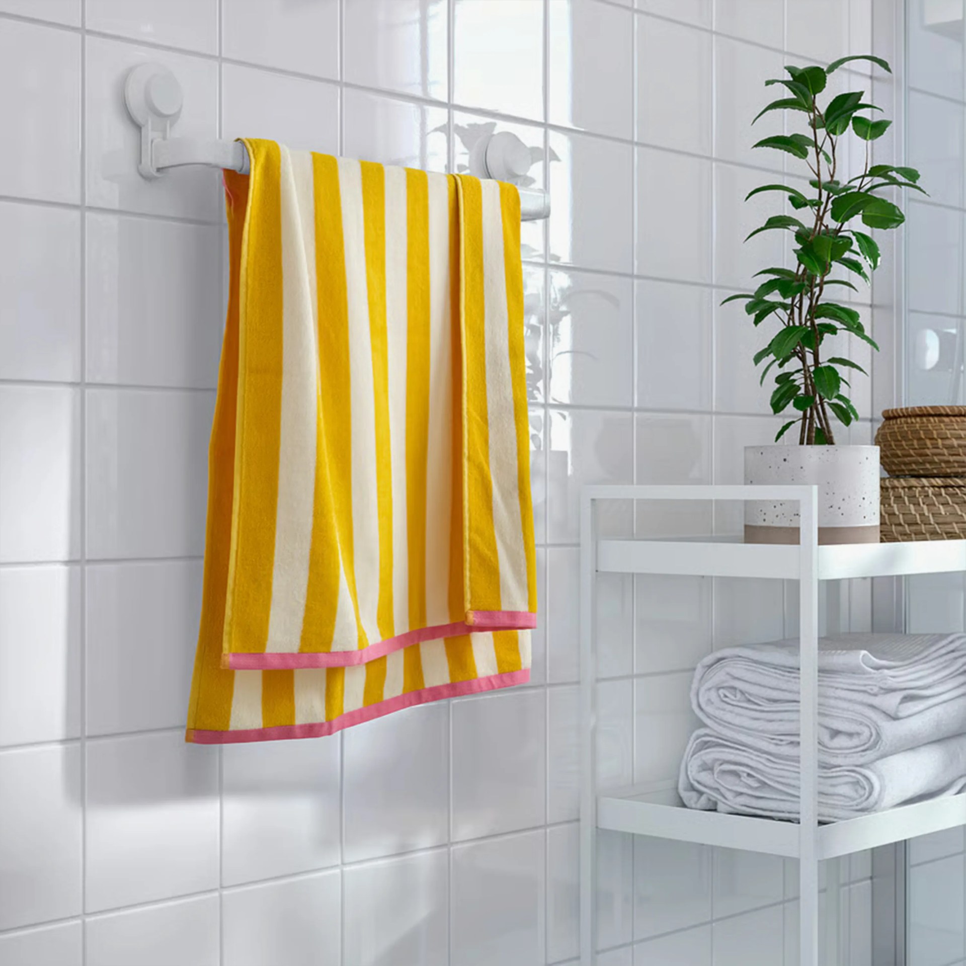 Yellow and white striped towel with pink edges hanging on a white towel rack against tiled wall.