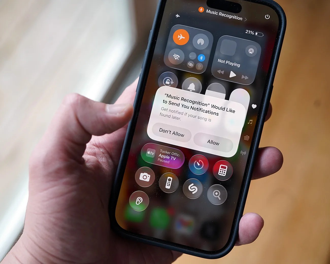 Hand holding a smartphone displaying a notification asking to allow Music Recognition to send notifications.