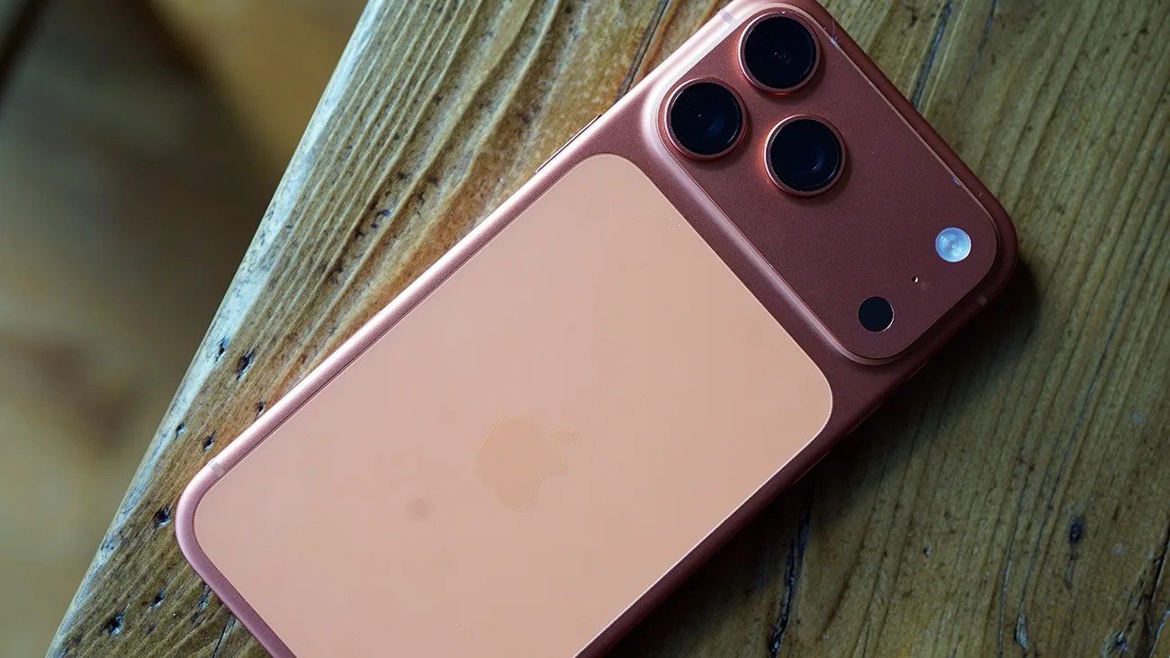 Rose gold iPhone with triple camera lenses on a wooden surface.