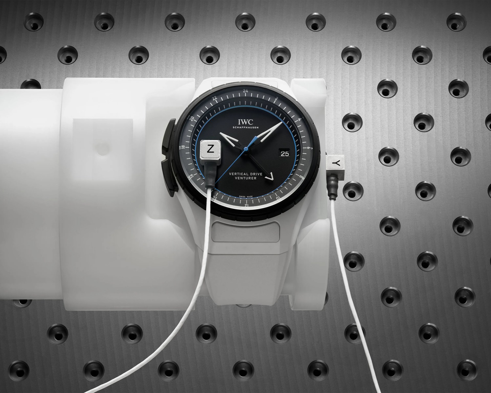 Black dial IWC Schaffhausen Vertical Drive Venturer watch with white strap on a white wrist model against a perforated metal background.