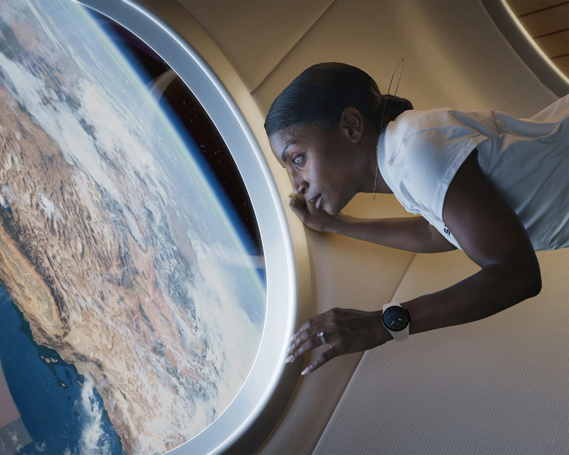 Person in a white shirt wearing a smartwatch looking out a large circular window at Earth from space.