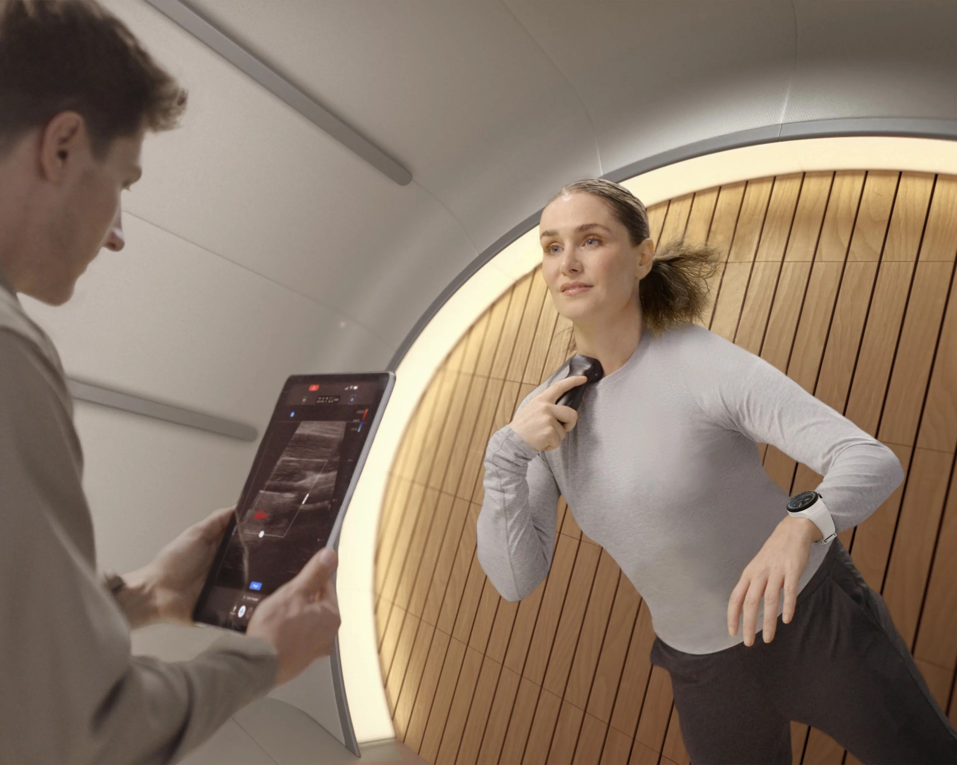 Woman using a handheld ultrasound device on her neck while a man views the scan on a tablet in a modern room.