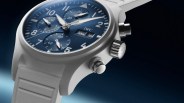 White IWC chronograph watch with blue dial, silver hands, and white rubber strap against a dark gradient background.